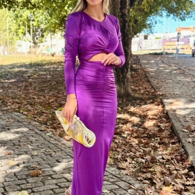 Mulher com vestido roxo acetinado e mala floral em passeio de outono
