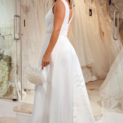 Mulher de vestido branco de noiva com cinto de pérolas e bouquet na mão numa loja de vestidos de noiva