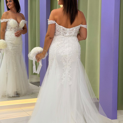 Mulher com vestido de noiva branco com renda e tule diante de espelho e paredes lilás e verdes