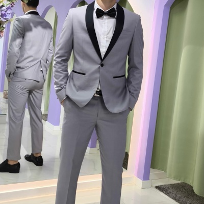 Homem com fato cinzento e gravata borboleta preta num ambiente com arco de flores e cortina verde