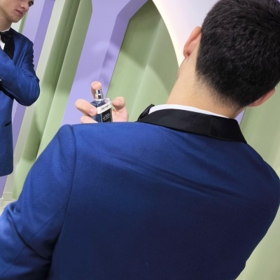 Homem a usar perfume 'BLACK FOR MEN' à frente de um espelho com arco de flores