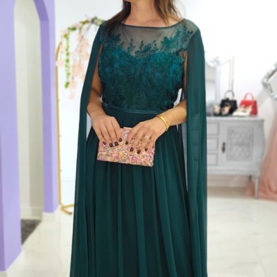 Mulher com vestido longo verde escuro bordado segurando carteira colorida em ambiente interno