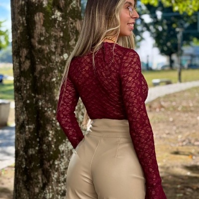 Mulher de costas com blusa de renda vinho e shorts bege ao ar livre