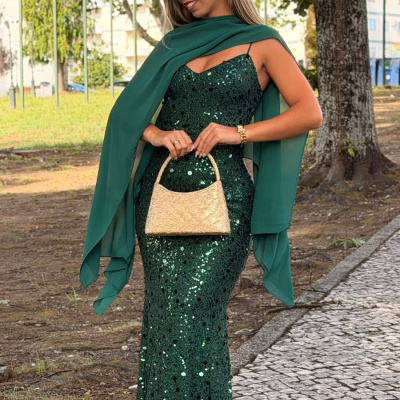 Mulher com vestido verde de lantejoulas e lenço, segurando mala dourada em exterior