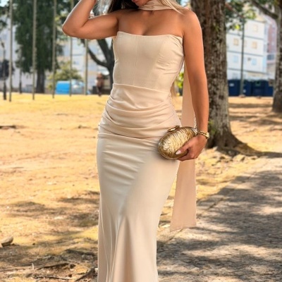 Mulher com vestido longo crema e clutch dourada ao ar livre