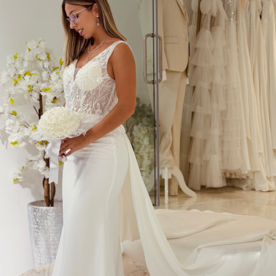 Vestido de noiva branco rendado com buquê e cauda longa numa loja.