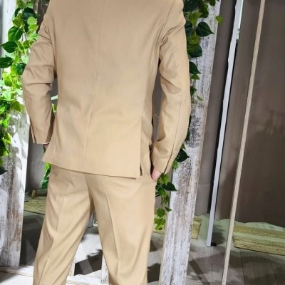 Homem de costas com fato bege e sapatos brancos em ambiente interior com espelho e plantas verdes