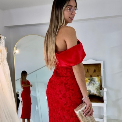 Mulher de vestido vermelho com clutch dourada em interior com espelho e cadeira branca
