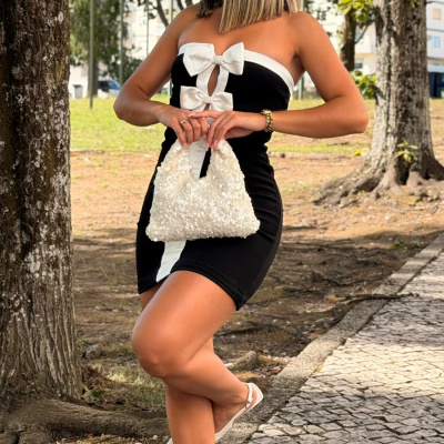 Mulher com vestido preto e branco, sapatos brancos, mala branca segurando ao ar livre junto a árvores