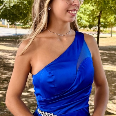 Vestido azul royal de um ombro só com cinto de pedras brilhantes e clutch branca ao ar livre