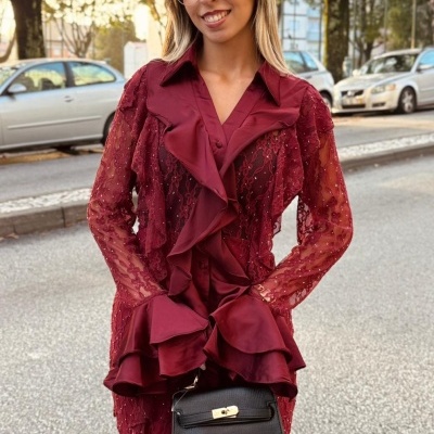 Mulher com vestido vinho rendado e babados segurando bolsa preta com fecho dourado na rua