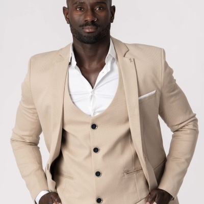 Homem a usar fato bege composto por casaco, colete e calças, com camisa branca e fundo neutro claro