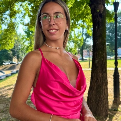 Mulher a usar vestido rosa com decote drapeado num parque com árvores.