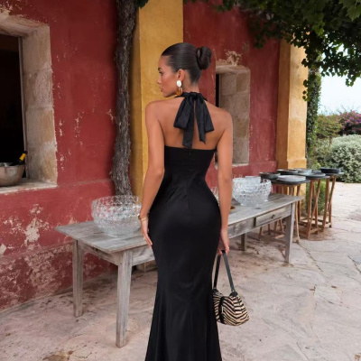 Mulher de costas com vestido preto longo e laço, segurando mala zebra, em exterior com parede vermelha e amarela