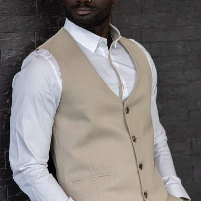 Homem de pele escura com colete bege e camisa branca encostado numa parede preta