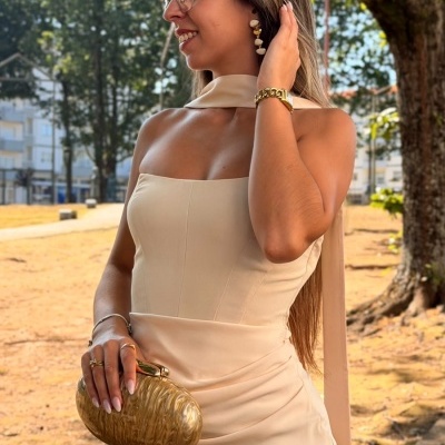 Mulher com vestido azul claro e mala dourada ao ar livre