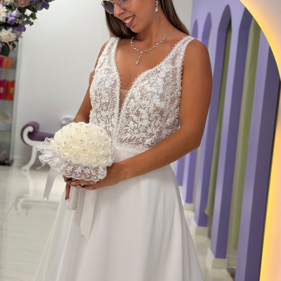 Mulher de vestido de noiva branco com corpete em renda com bouquet branco em estúdio decorado.