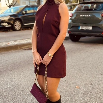 Mulher com vestido bordô e botas pretas a andar na rua com bolsa de corrente dourada