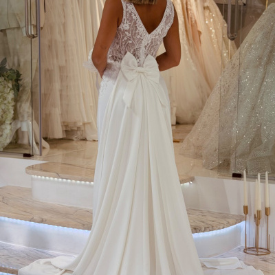 Vestido de noiva branco com laço e renda, visto por detrás, numa loja de vestidos.