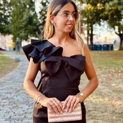 Mulher de vestido preto com babados e carteira bege ao ar livre