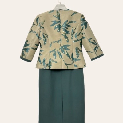 Conjunto feminino bege com padrão de folhas e saia verde escura pendurado.