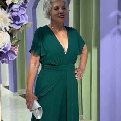 Mulher com vestido longo verde escuro e carteira branca em ambiente interno com paredes lilás e verde