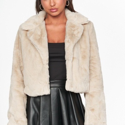 Mulher a usar casaco curto bege de pelo sintético com gola grande e saia preta de pele.