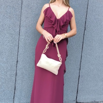 Vestido longo vinho com folhos e mala bege em fundo cinzento