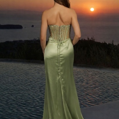 Mulher de costas a usar vestido verde oliva longo de cetim com pérolas, pôr do sol sobre mar e piscina