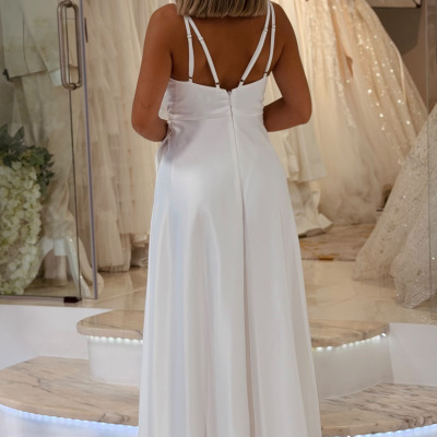 Mulher de costas a usar vestido branco longo com alças duplas, numa loja de vestidos de noiva.