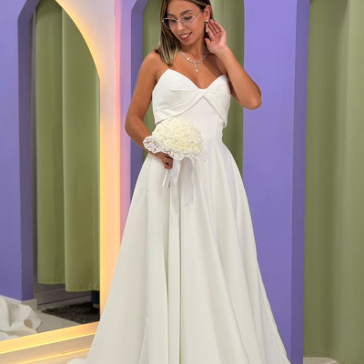 Jovem mulher com vestido de noiva branco segurando ramo de flores, com parede roxa e cortinas verdes ao fundo