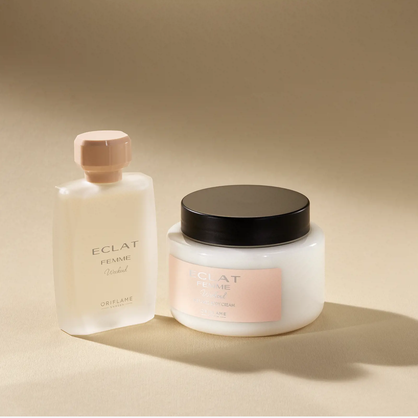 47014 Creme de Corpo Perfumado Eclat Femme Weekend Dois frascos de produtos de beleza Oriflame Eclat Femme Weekend sobre fundo bege.