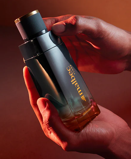 62542 MALBEC FLAME EAU DE TOILETTE, 100ML Frasco de perfume Mallecc Vintage nas mãos com fundo laranja