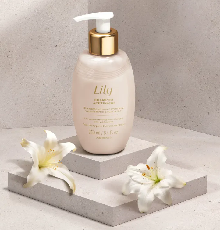 48511 SHAMPOO ACETINADO LILY, 250ML Frasco de shampoo acetinado Lily rosa com tampa branca e dourada sobre plataforma cinza com flores de lírio brancas