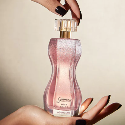 Frasco de perfume rosa brilhoso segurado por mãos femininas com unhas negras
