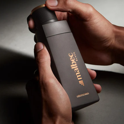 Frasco de perfume Malbec Black preto fosco segurado por mãos