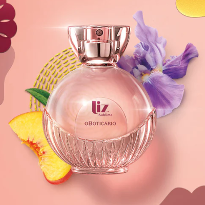 Frasco de perfume rosa com tampa metálica e flores e pêssego ao fundo