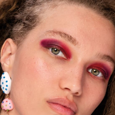 Rosto de mulher com sombra rosa-avermelhada e brincos pendentes coloridos