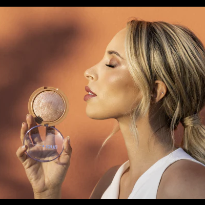 Mulher loira segura compacto de maquilhagem dourado com tampa transparente e texto 'FENTY'