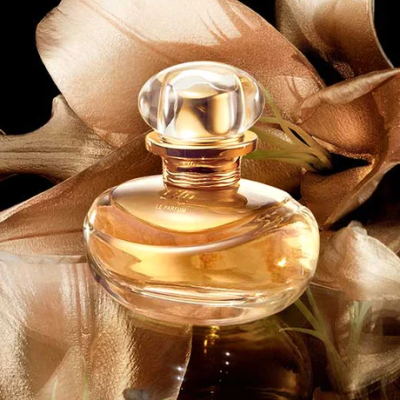 Frasco de perfume em vidro com líquido dourado e flores douradas ao fundo
