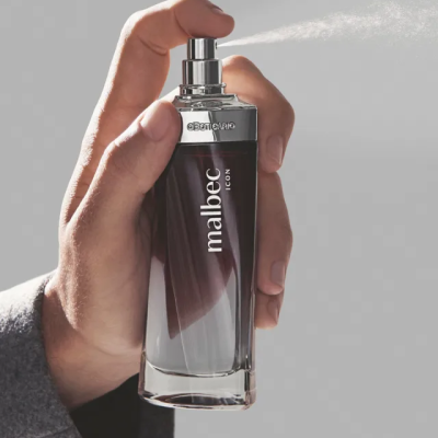 Frasco de perfume Malbec Icon segurado por uma mão num fundo cinzento