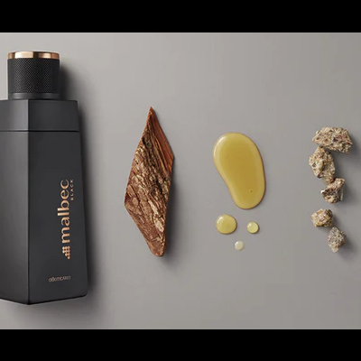 Frasco preto malbec com tampa e gotas de líquido ao lado sobre fundo cinza