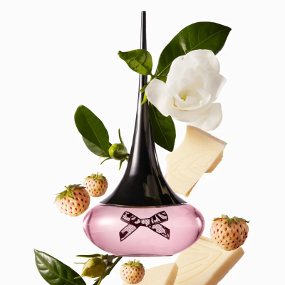 Frasco de perfume rosa com tampa preta, rodeado por folhas, flores brancas e chocolate branco.