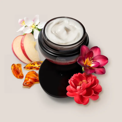 Creme cosmético em recipiente preto com flores, maçã e âmbar ao redor