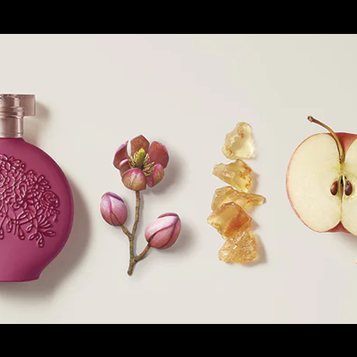 Frasco de perfume rosado com frutas e cristais sobre fundo bege