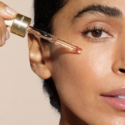 Mulher aplicando sérum facial com conta-gotas dourado