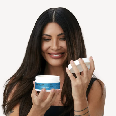 Mulher com creme em pote branco de tampa azul e rótulo azul