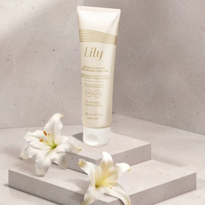 Frasco branco de sérum leave-in Lily com texto dourado, sobre degraus de pedra clara com dois lírios brancos ao lado