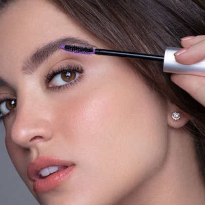 Mulher a aplicar rímel preto na sobrancelha com escova prateada