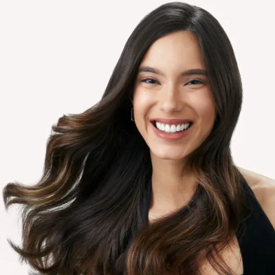 Mulher com cabelo castanho escuro longo e ondulado, roupa preta e fundo branco